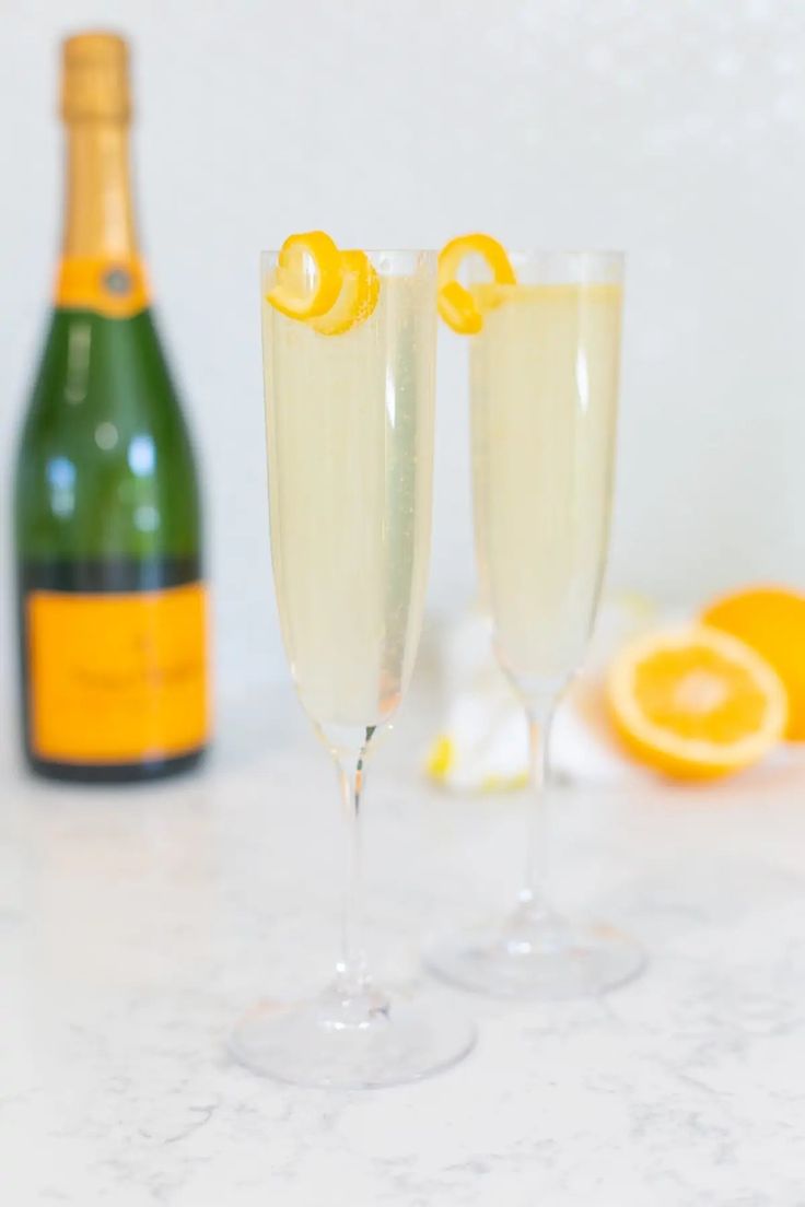 two champagne flutes with orange peels next to a bottle of wine and an orange slice