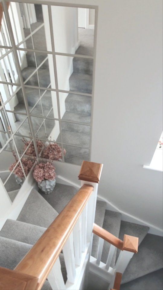 a mirror on the wall next to a stair case and vase with flowers in it