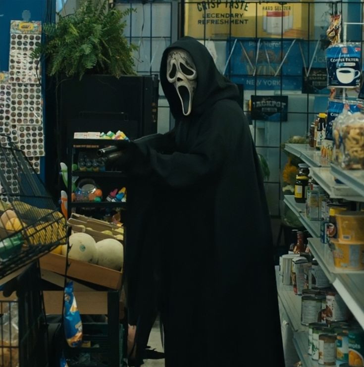 a person in a skeleton mask and black hood is shopping at a grocery store with an empty cart