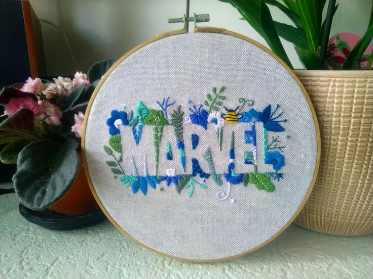 a close up of a embroidery on a table next to a potted plant with flowers