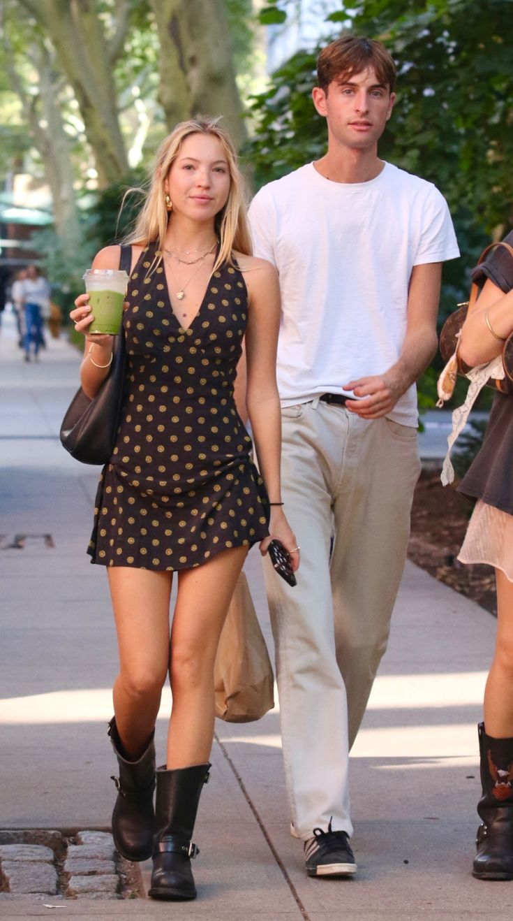 a man and woman walking down the street with coffee in their hands, one holding a drink