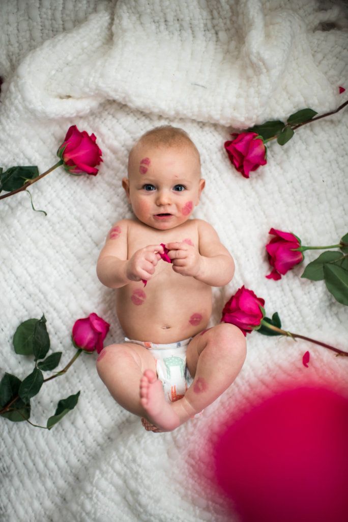 a baby sitting on top of a blanket next to pink flowers and leaves with one hand in his mouth