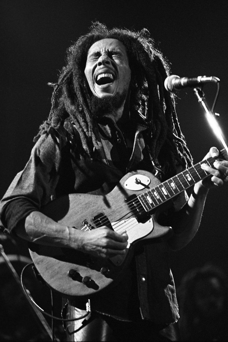 a man with dreadlocks playing a guitar and singing into a microphone on stage