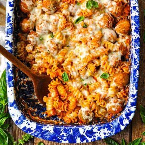 a casserole dish filled with pasta, meatballs and cheese on a wooden table