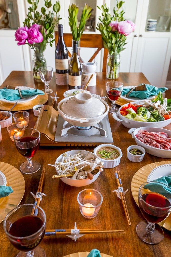 a wooden table topped with plates and bowls filled with food next to bottles of wine