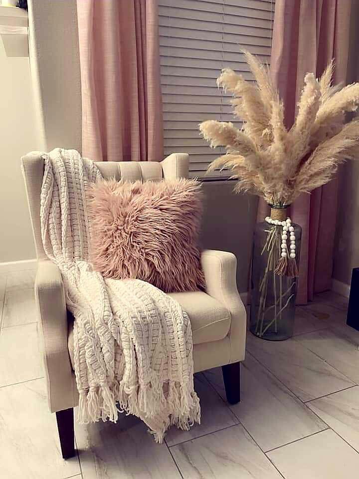 a chair with a blanket on it next to a vase filled with dried grass and a throw pillow