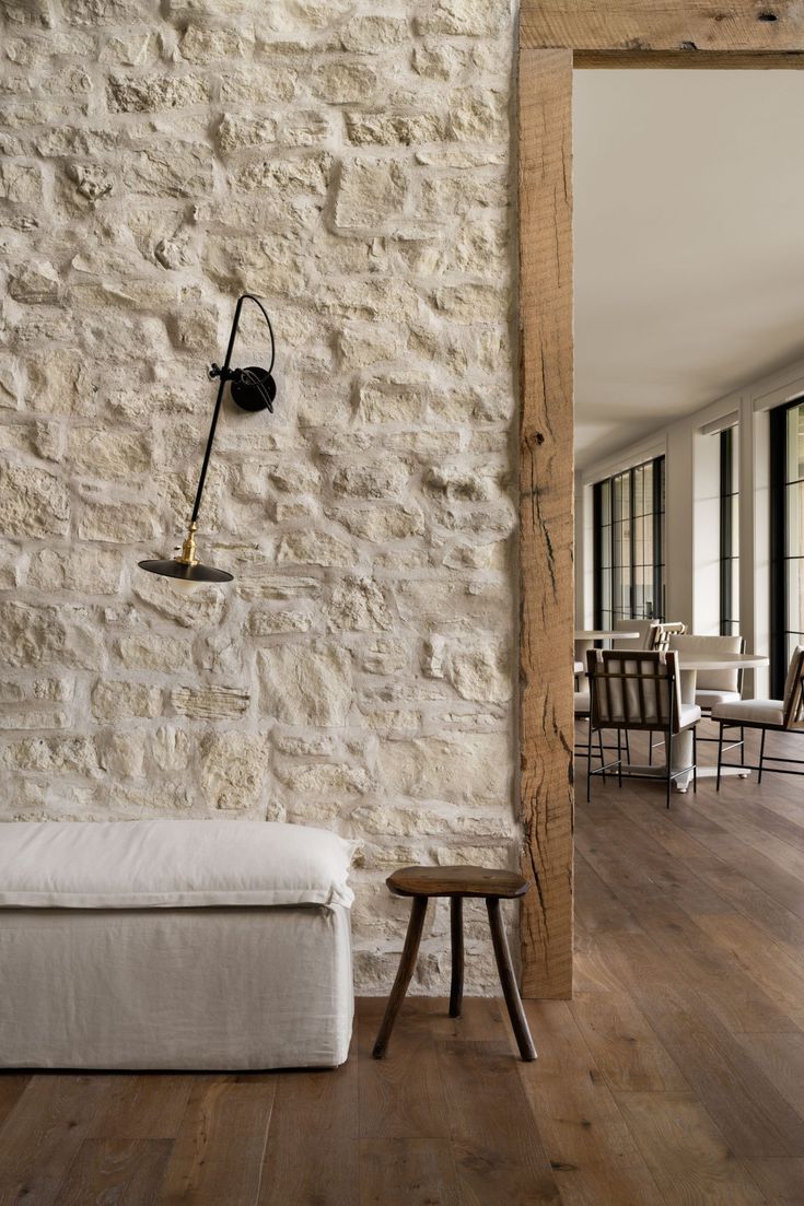 a white couch sitting in front of a stone wall next to a wooden table and chairs