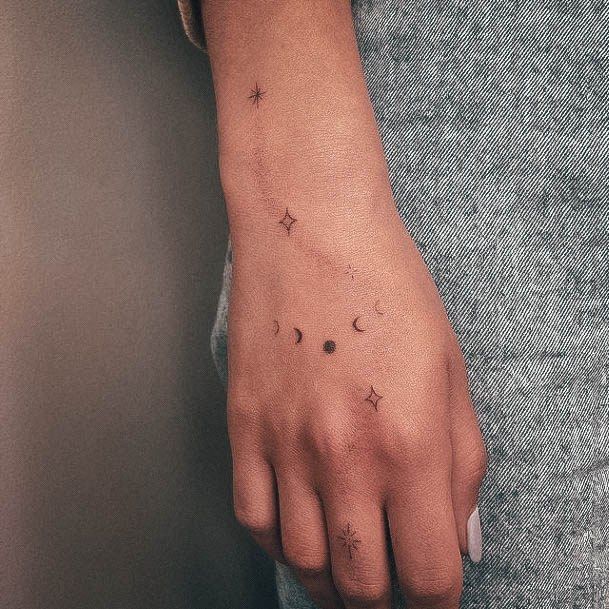 a woman's hand with small stars and moon tattoos on her left wrist,