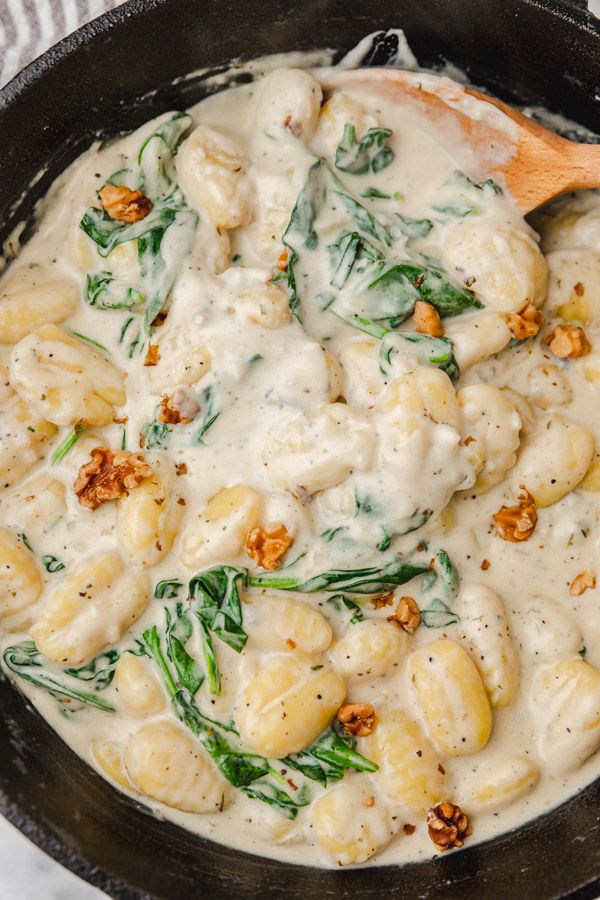 a skillet filled with ravioli and spinach covered in white sauce on top of a table