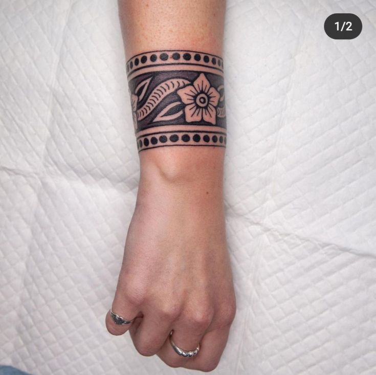 a woman's arm with a black and white tattoo design on the left wrist