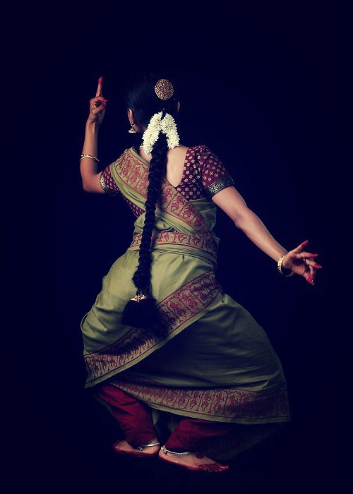 a woman in a green and red sari dancing with her hands out to the side