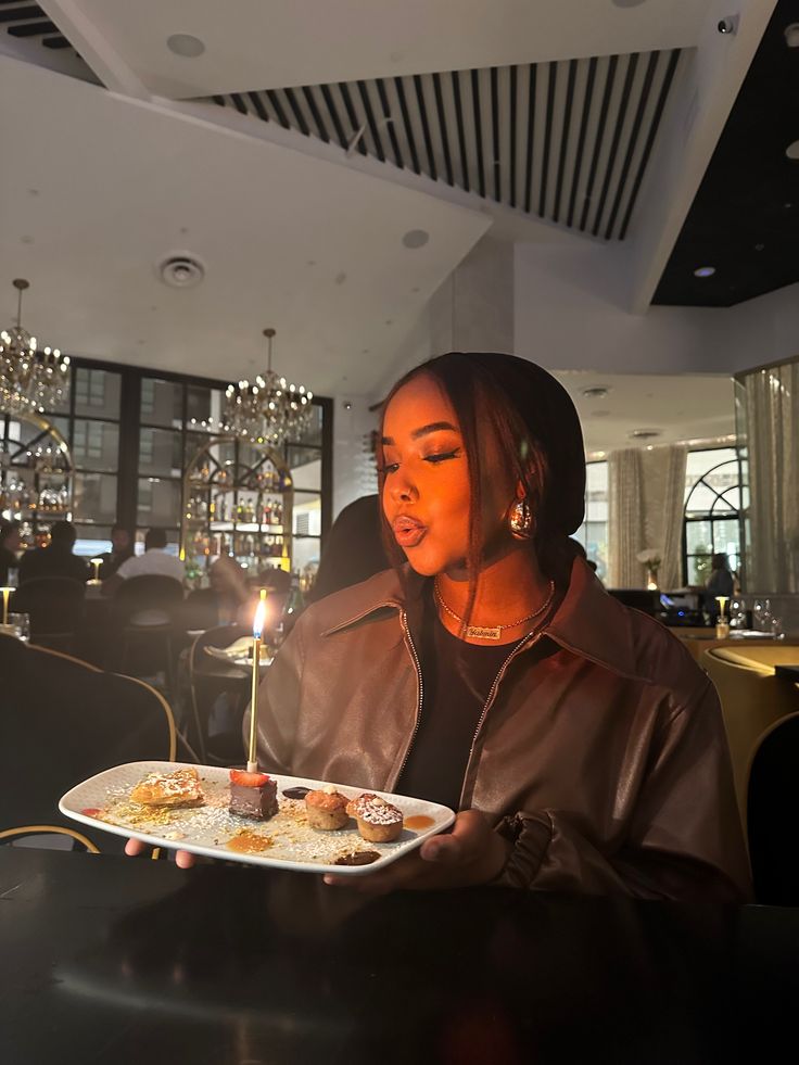 a woman sitting at a table holding a plate with donuts on it and a candle in her hand