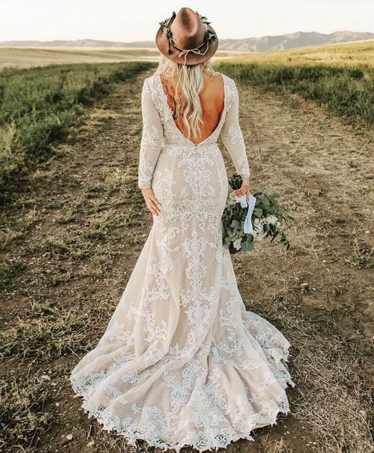 a woman in a wedding dress and cowboy hat walking down a dirt road with her back to the camera