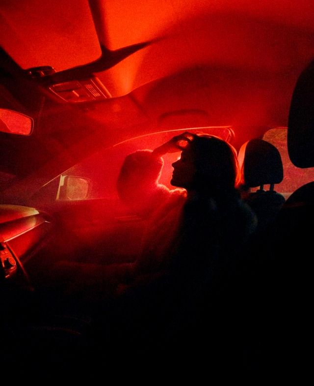 two people sitting in the back seat of a car with red light coming from behind them