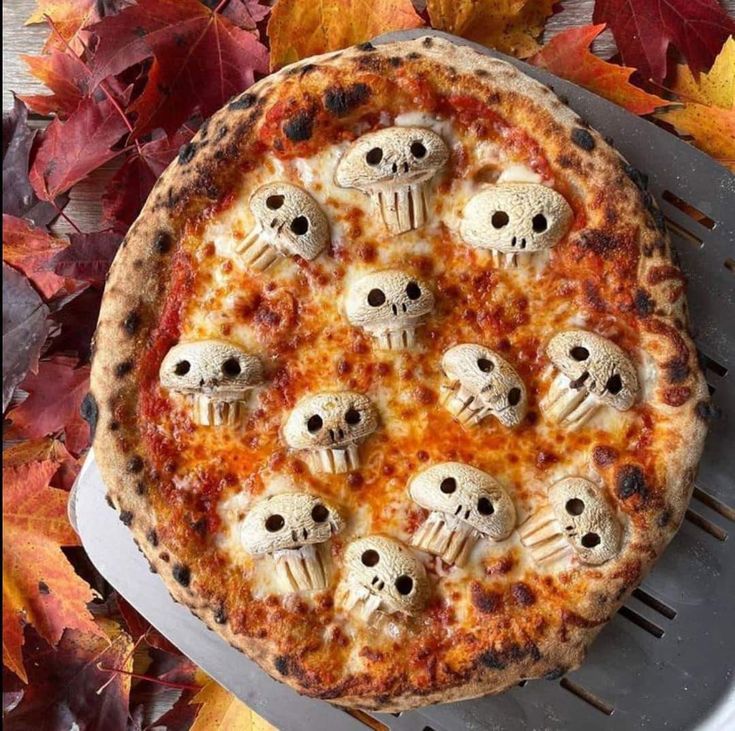 a pizza topped with lots of skulls on top of a metal rack next to leaves