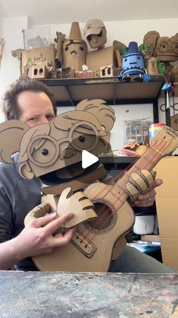 a man is holding up a guitar made out of cardboard and some paper machs