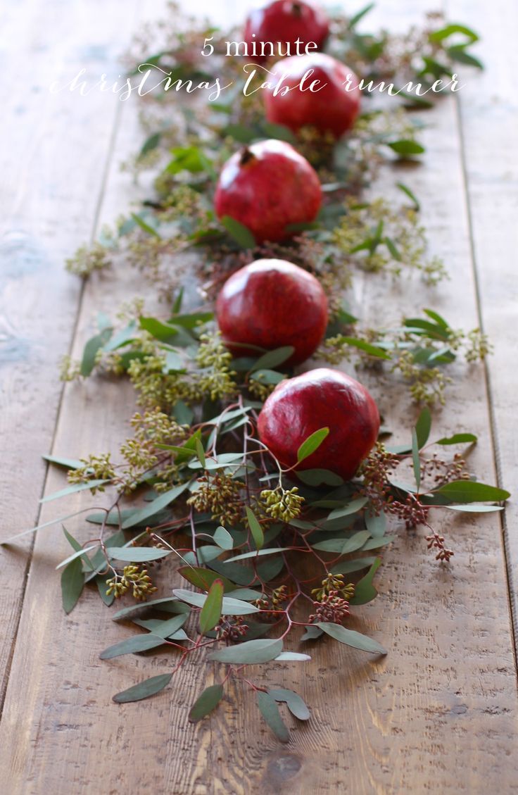 three apples are lined up on a wooden table with leaves and greenery around them