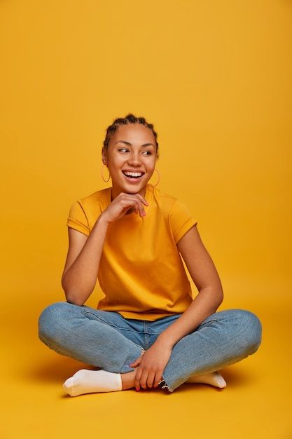 a woman sitting on the floor with her legs crossed, smiling and looking at the camera