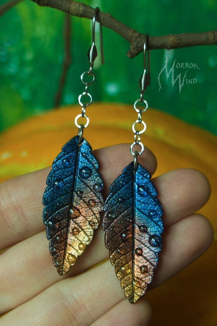 a pair of blue and gold leaf earrings on a tree branch in front of a green background