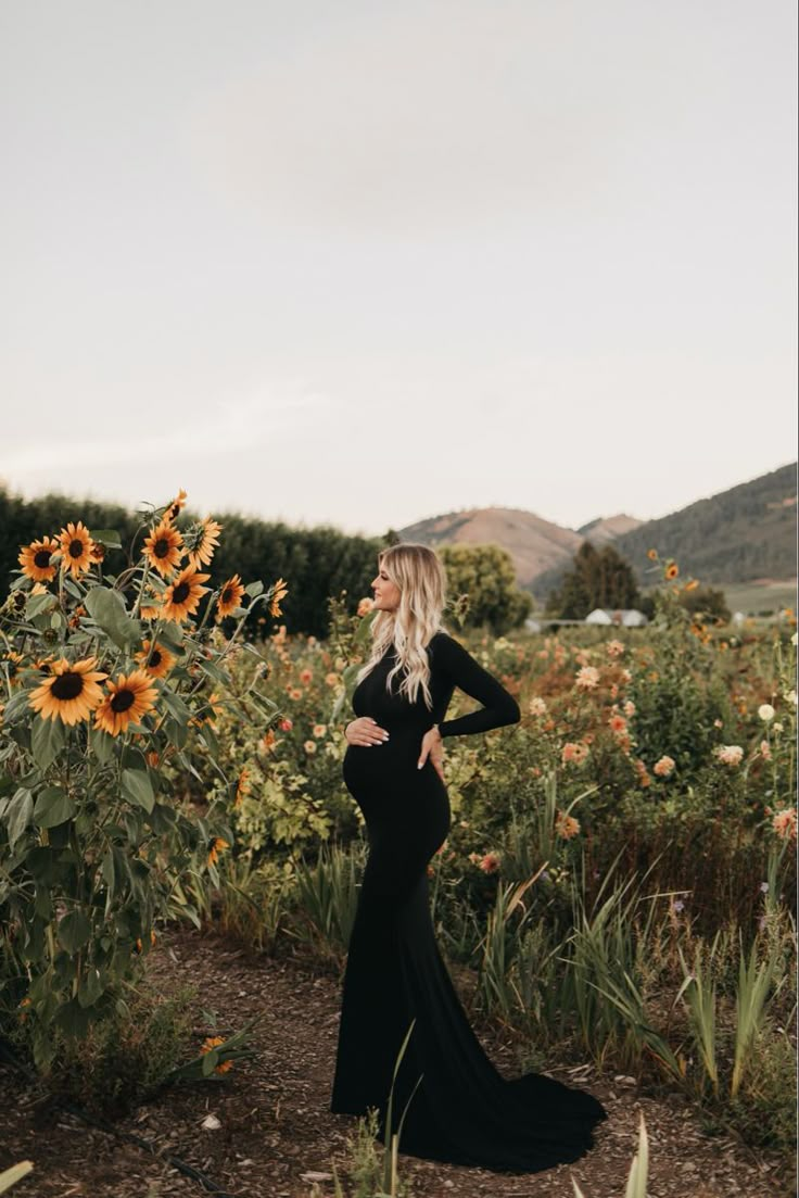 a pregnant woman in a black dress standing in a field with sunflowers