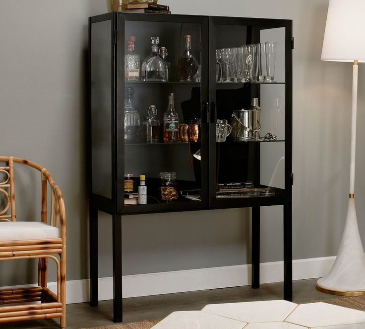 a bar cabinet with liquor bottles and glasses on the top shelf, next to a wicker chair