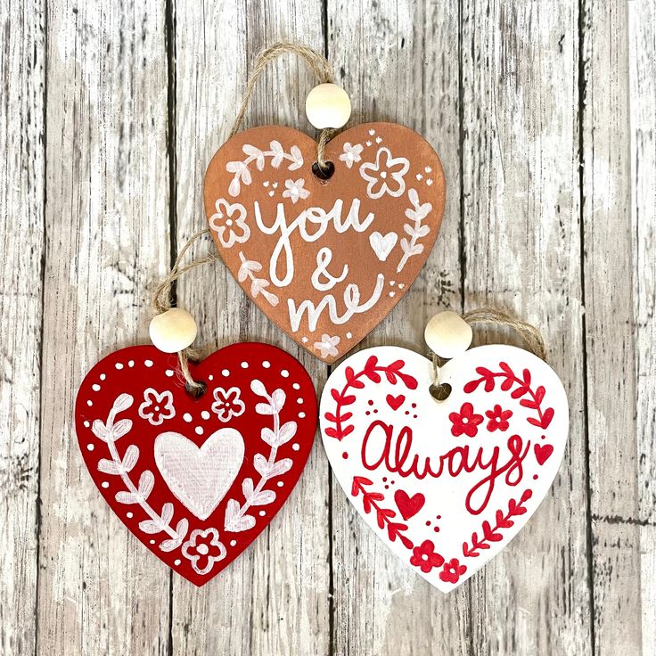 three heart shaped ornaments hanging from string on wooden background with words you & me and always