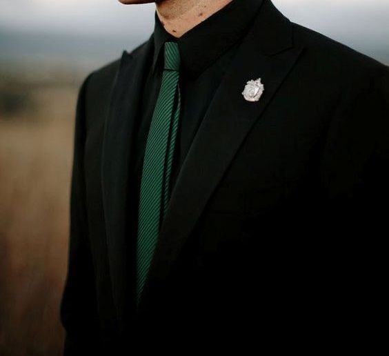 a man in a black suit and green tie with a badge on his lapel