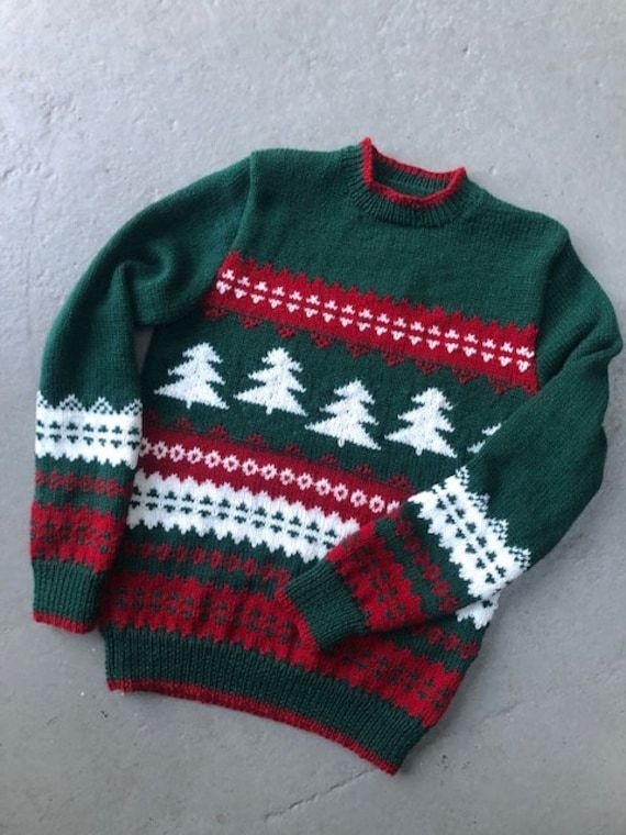 a green sweater with red and white christmas trees on the front, sitting on a concrete floor