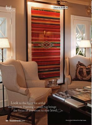 a living room with two chairs and a rug hanging on the wall above the couch