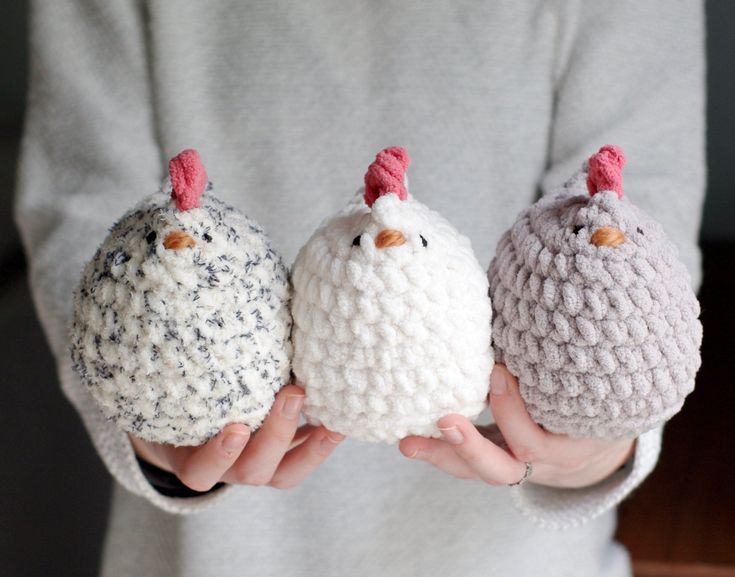 three crocheted chickens are held in their hands, one is wearing a gray sweater