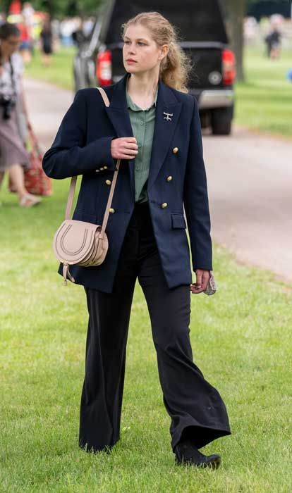 a woman is standing in the grass with her hand on her hip and holding a purse