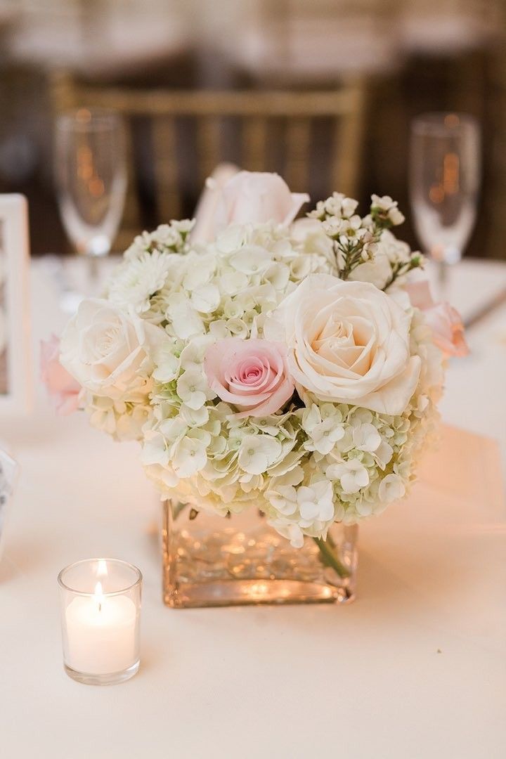 a vase filled with white and pink flowers sitting on top of a table next to a candle