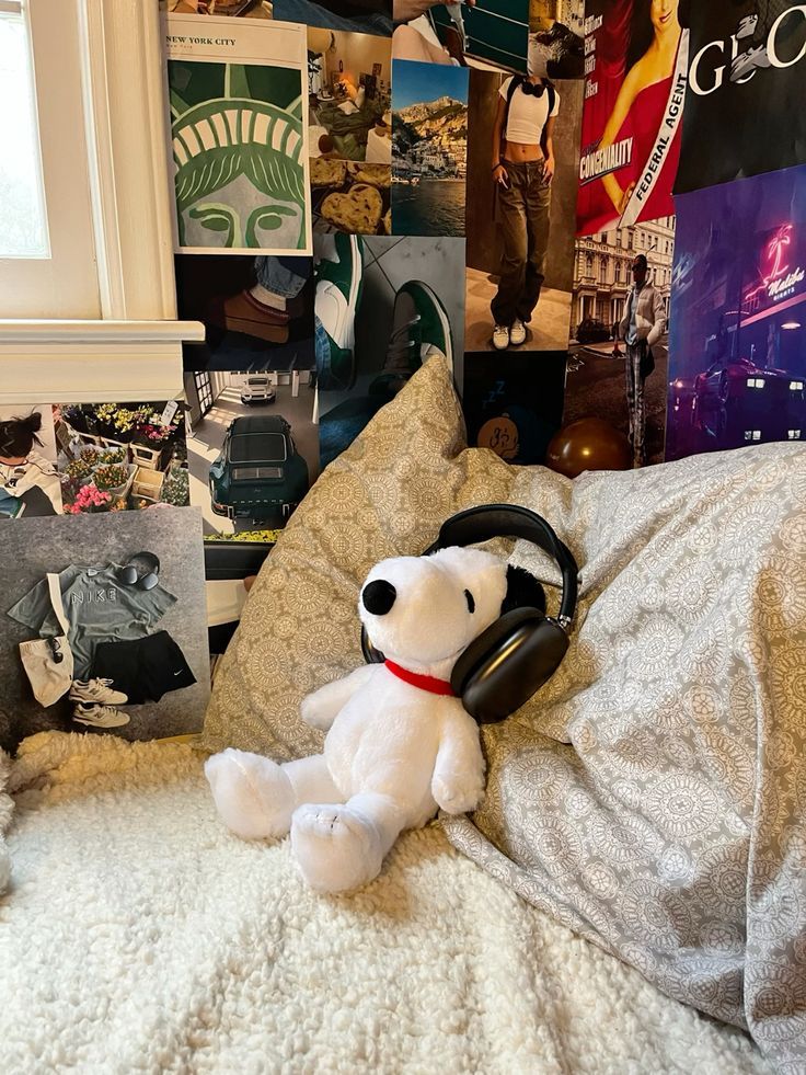 a teddy bear with headphones sitting on a bed in front of a wall full of posters