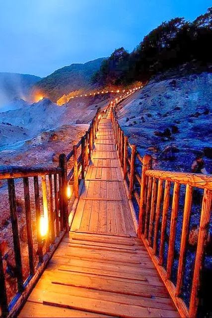 a wooden walkway leading to the ocean at night with lanterns lit up on it's sides