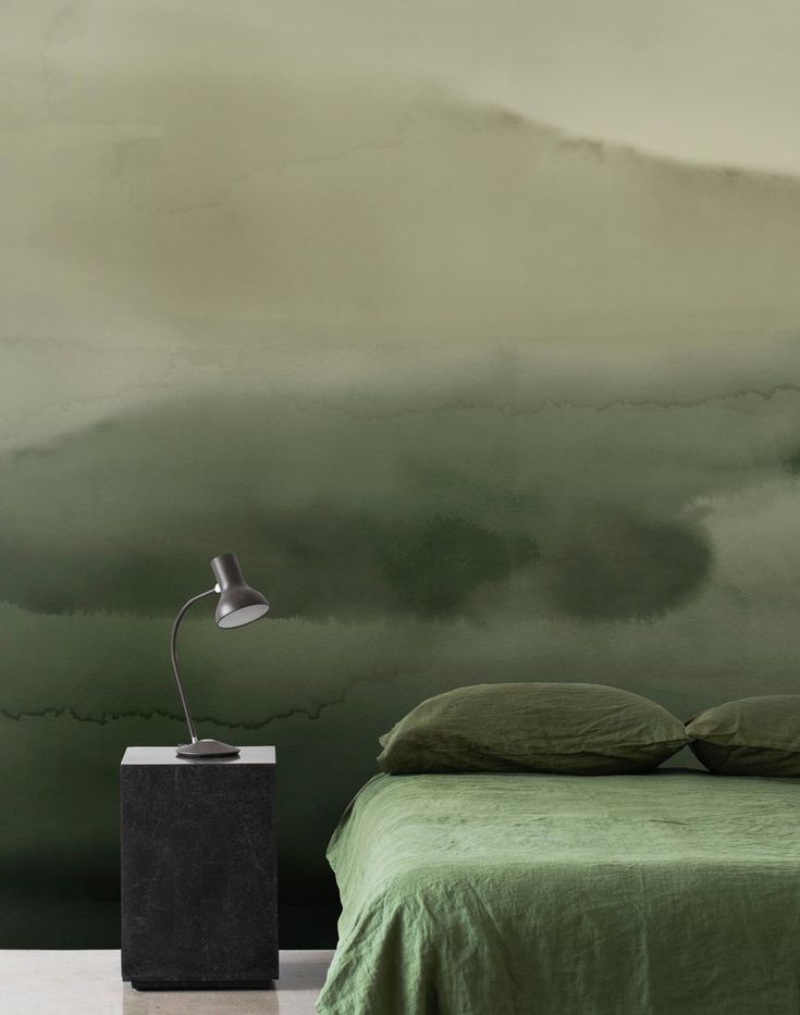 a bedroom with green bedding and a painting on the wall next to a night stand