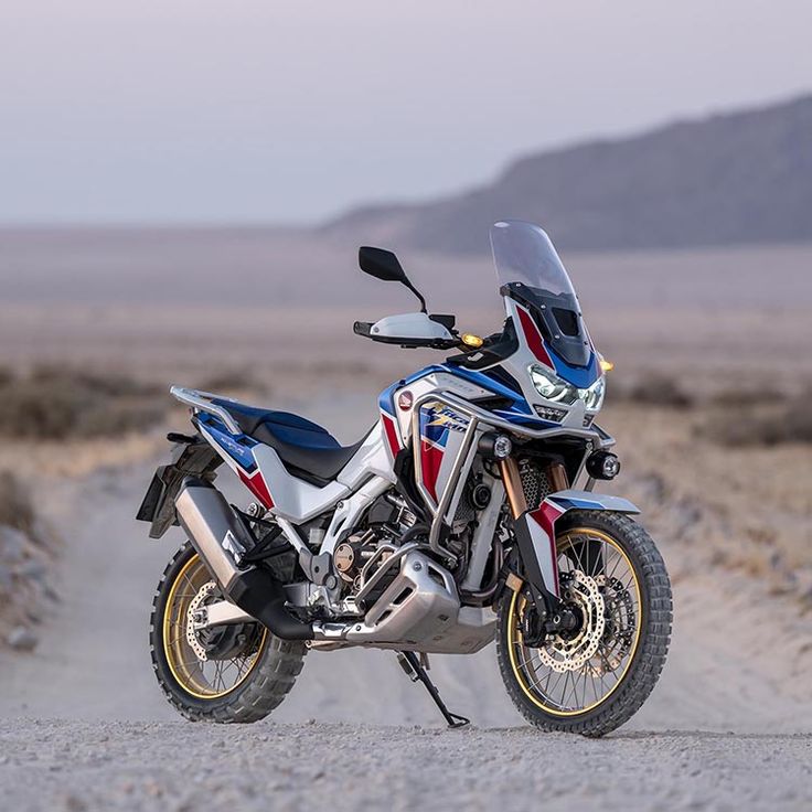 a red, white and blue motorcycle parked on the side of a road in the desert