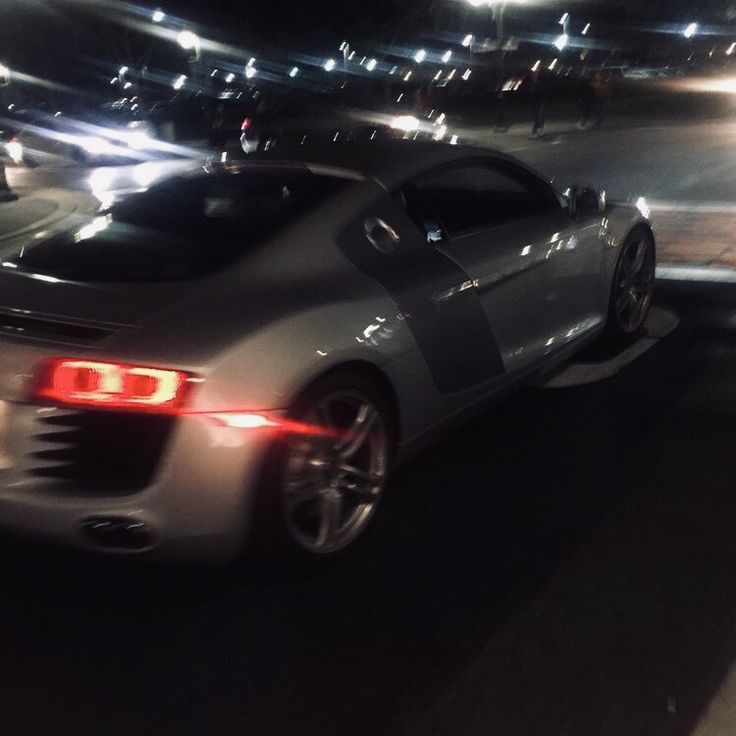 a silver sports car driving down a street at night time with lights on and cars behind it