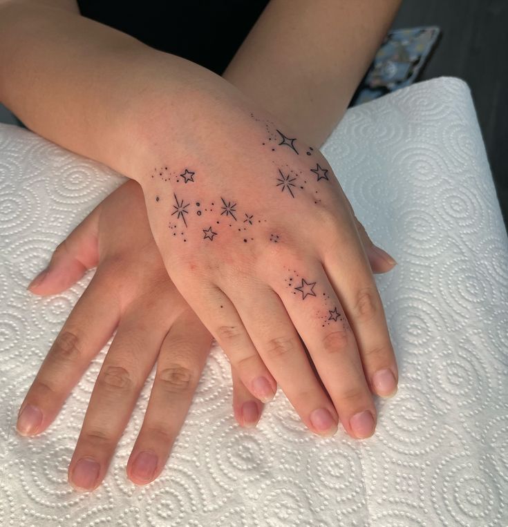 a woman's hand with stars tattooed on it sitting on top of a bed