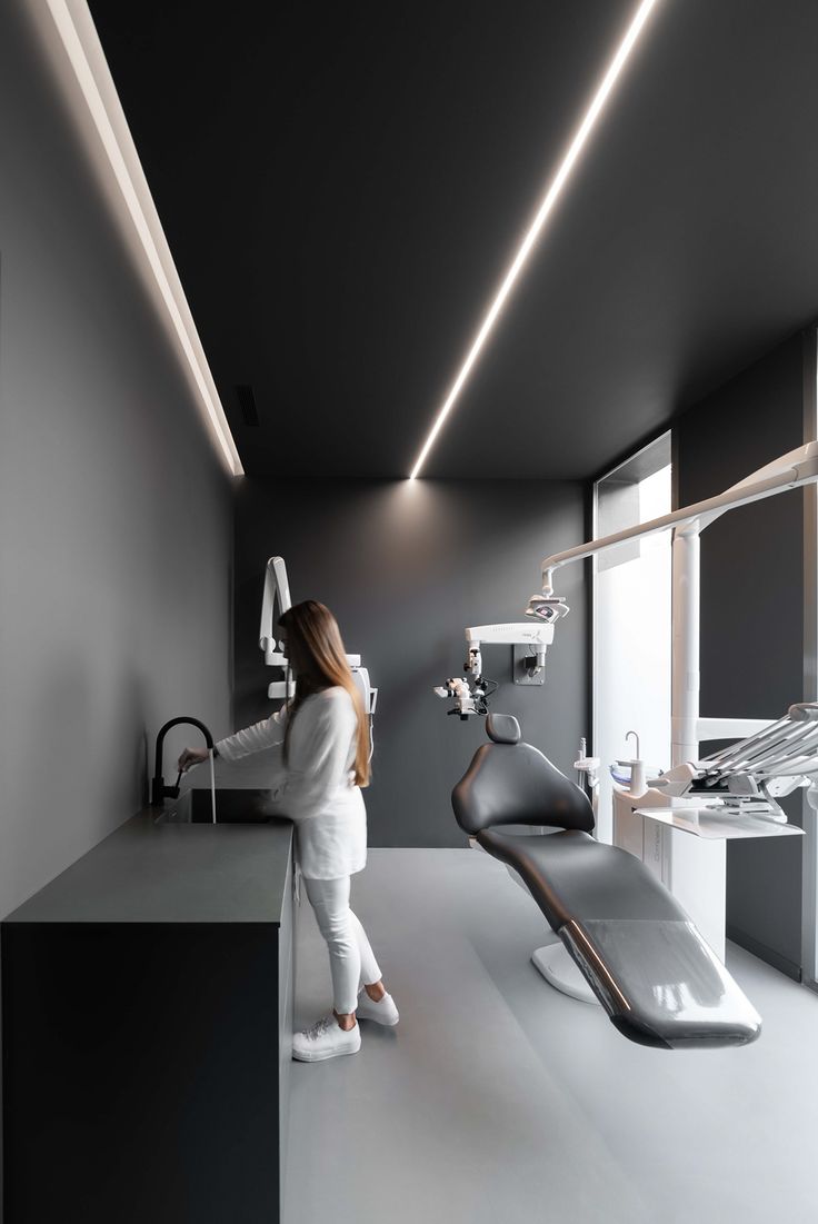 a woman standing in front of a dentist's chair next to a sink and mirror