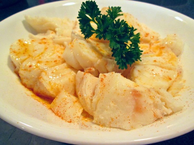 a white plate topped with fish covered in gravy and garnished with parsley