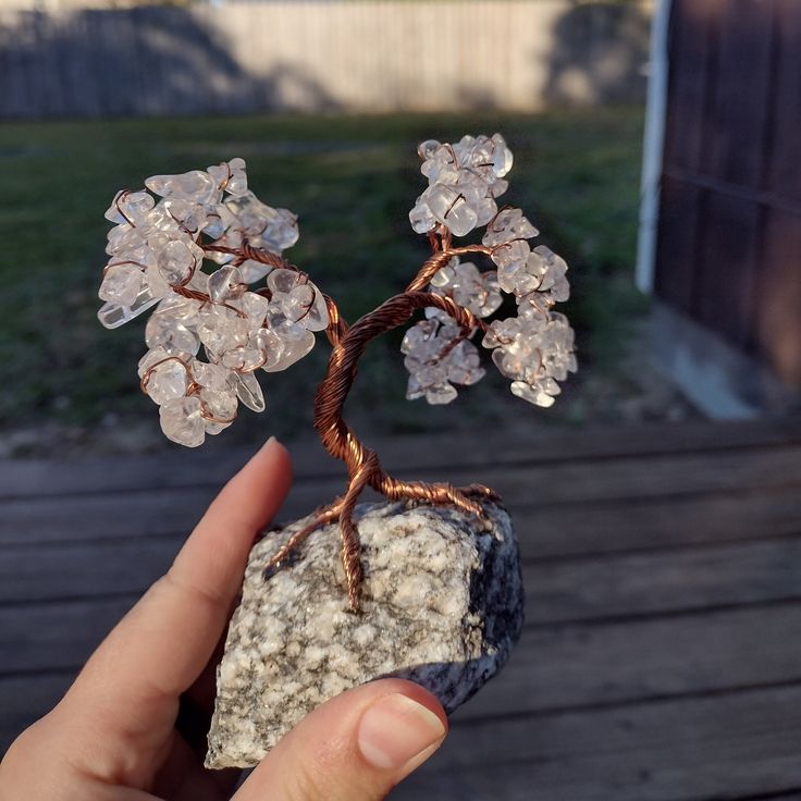 a hand holding a rock with a wire tree on it