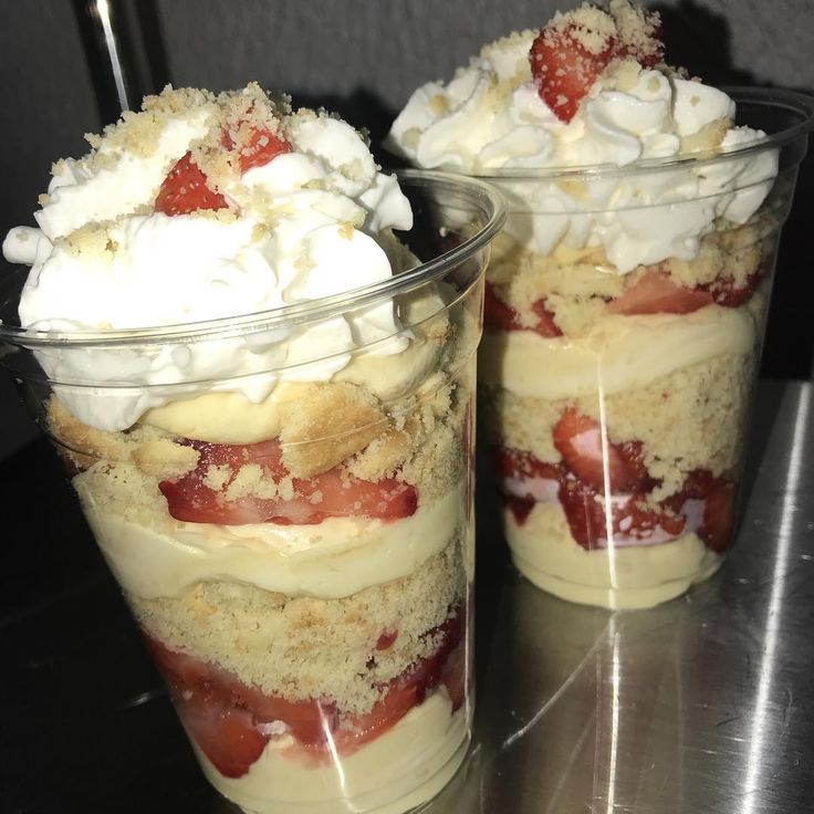 two desserts in plastic cups with strawberries and whipped cream