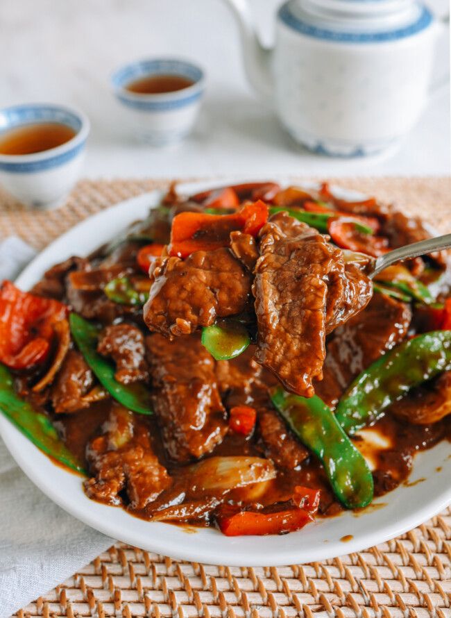 a white plate topped with meat and veggies next to two cups of tea