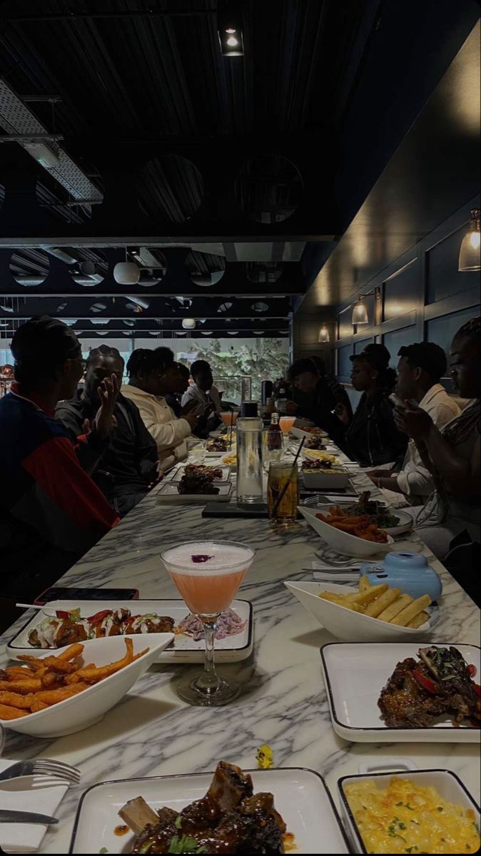 many people are sitting at a long table with plates of food in front of them