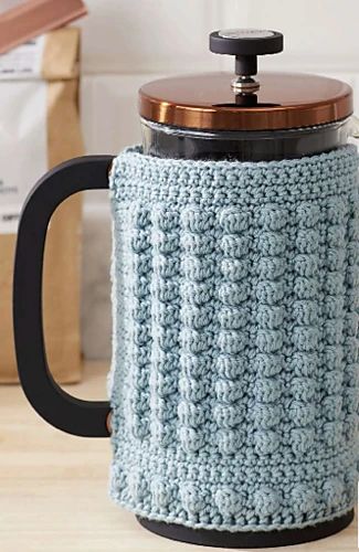 a blue crocheted coffee pot cozys up with a wooden lid on a table