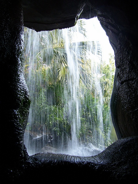 the inside of a cave with water cascading down it's face and trees in the background