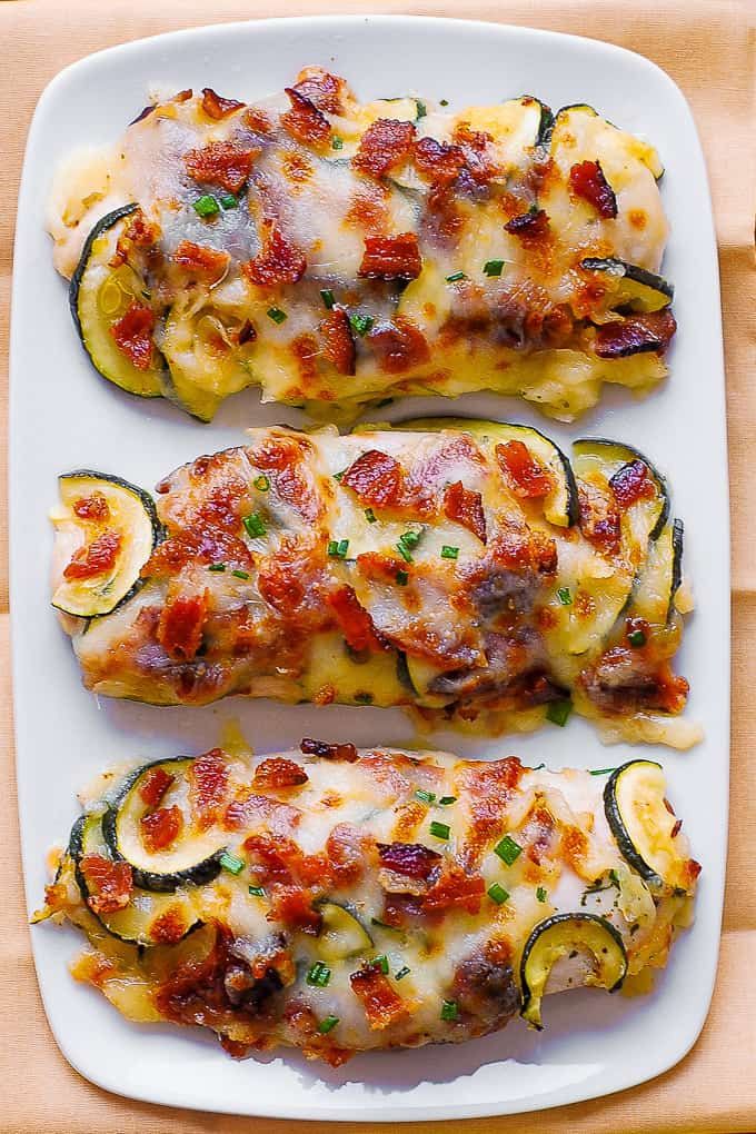 zucchini stuffed with meat and cheese on a white platter next to an orange napkin