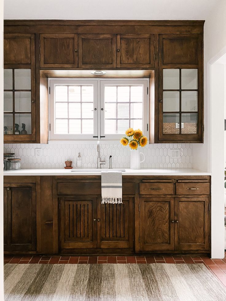 a kitchen with wooden cabinets and white counter tops, sunflowers on the window sill