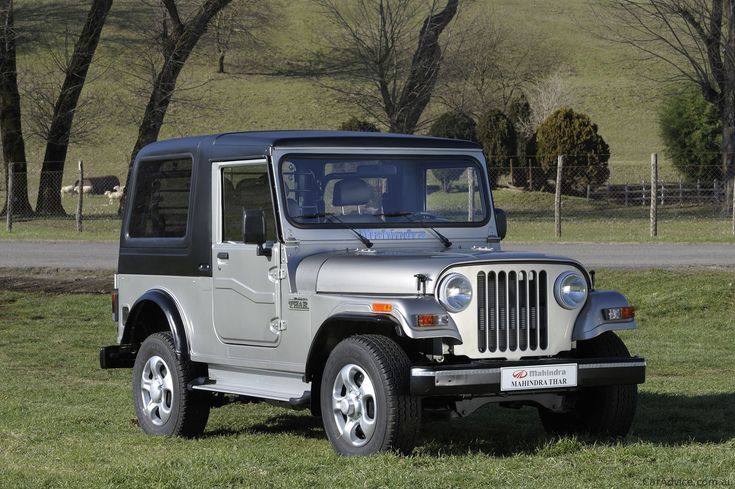 a silver jeep parked in the grass near a road