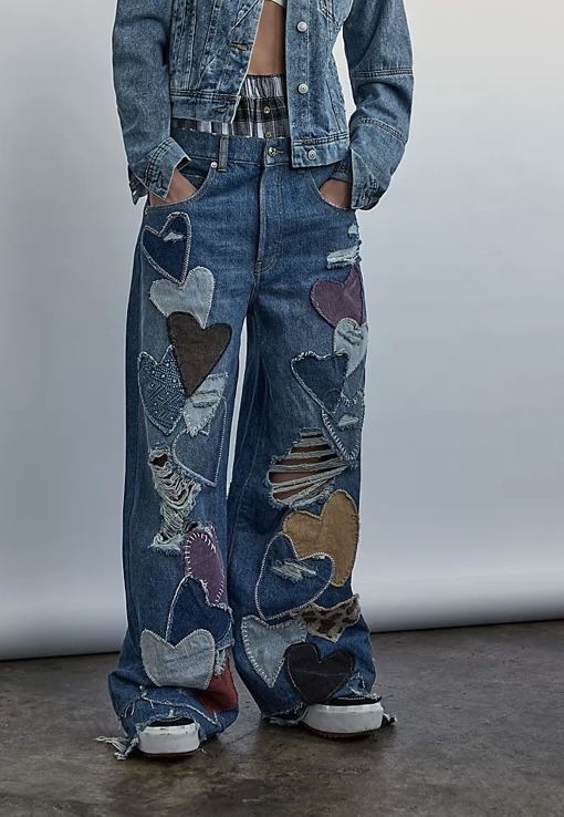 a woman standing in front of a white wall wearing ripped jeans and a jean jacket